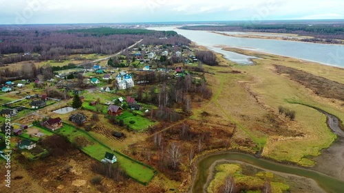 Aerial view of the village on a high hill above the river at sunrise in autumn. Aerial view. Residential buildings and a church, river bends, meadows, orange grass, trees at dawn. Colorful aerial land