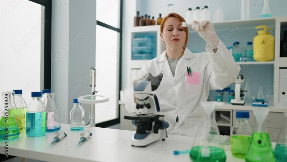 Young redhead woman wearing scientist uniform using microscope working at laboratory Young redhead woman wearing scientist uniform using microscope working at laboratory