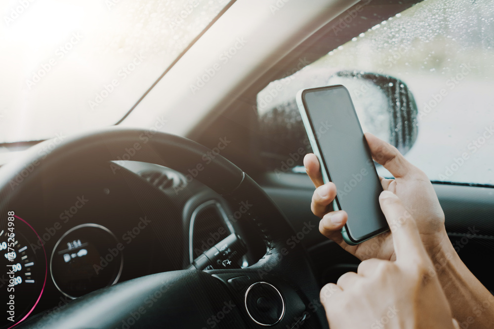 Hand of woman on steering wheel drive a car while using smartphone.