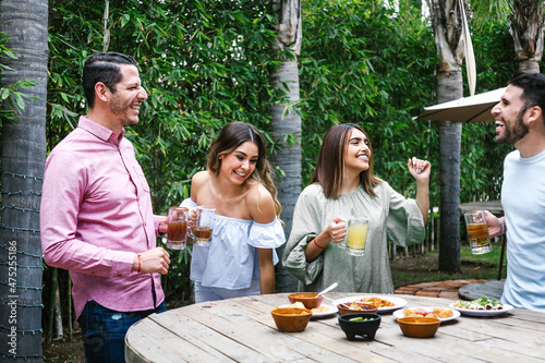 Group of young latin friends meeting for beer, michelada drinks and mexican food making a toast in restaurant terrace in Mexico Latin America photo