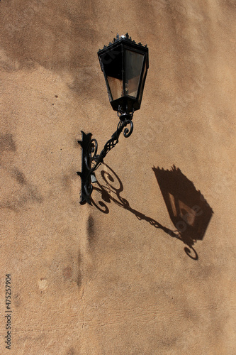 A black metal lantern in Colonial style on the wall, which casts a bright shadow during the day.