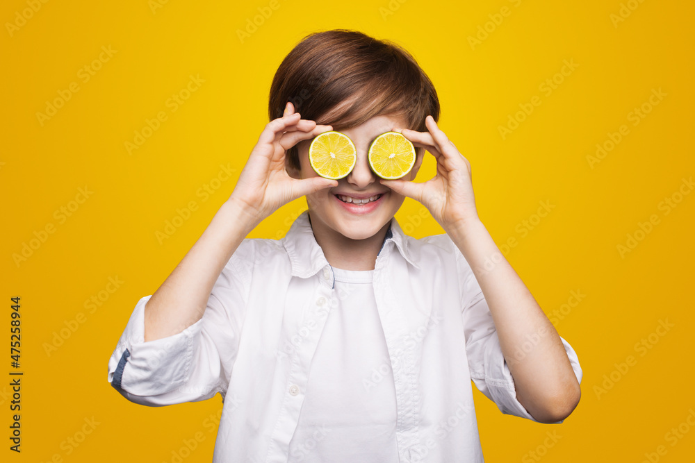 Portrait of a caucasian boy covering his eyes with lemons and smile isolated on a yellow studio wall. Lemon slices. Portrait of a caucasian boy covering his eyes with lemons and smile isolated on a yellow studio wall. Lemon slices.