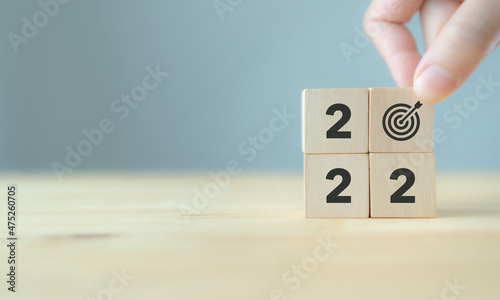 Business goals in 2022 concept. Goals achievement. Hand puts wooden cutes with goals, target icon on grey background. Start new year 2022 with common goals, business vision, planning and strategies.