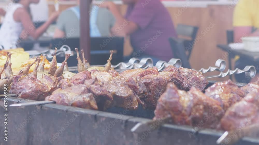 Juicy Appetizing Pork Kebab is Cooking in the Smoke Outdoors. Grilling grilled meat on skewers, on hot coals on grill. Clients at a table in a summer cafe or restaurant are waiting for their lunch. Juicy Appetizing Pork Kebab is Cooking in the Smoke Outdoors. Grilling grilled meat on skewers, on hot coals on grill. Clients at a table in a summer cafe or restaurant are waiting for their lunch.