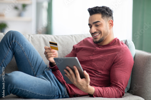 Cheerful arab man with credit card and digital tablet