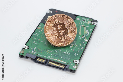 Copper colored physical bitcoin coin on the green backside of a SSD hard disk electrical circuits, white background