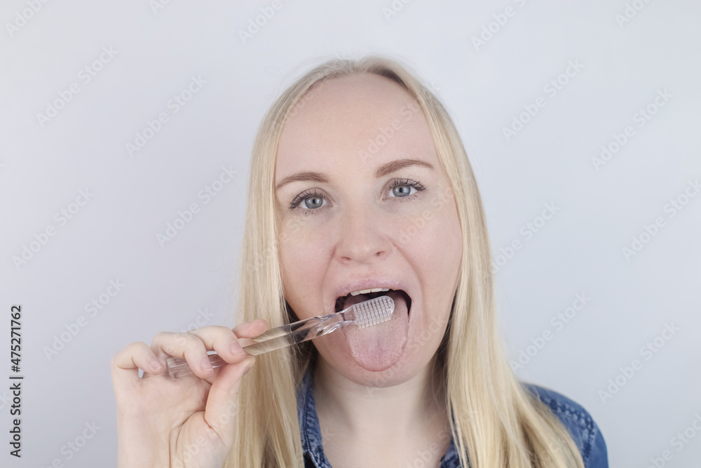 Clean tongue. Close-up of a woman performing antimicrobial hygiene with a special tongue brush. Isolated on white background. A blond female looks into the frame, as if he is looking in a mirror. Clean tongue. Close-up of a woman performing antimicrobial hygiene with a special tongue brush. Isolated on white background. A blond female looks into the frame, as if he is looking in a mirror.