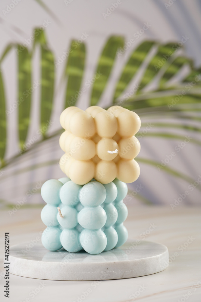One white square bubble candle on on top of one blue candle on a tropical background One white square bubble candle on on top of one blue candle on a tropical background
