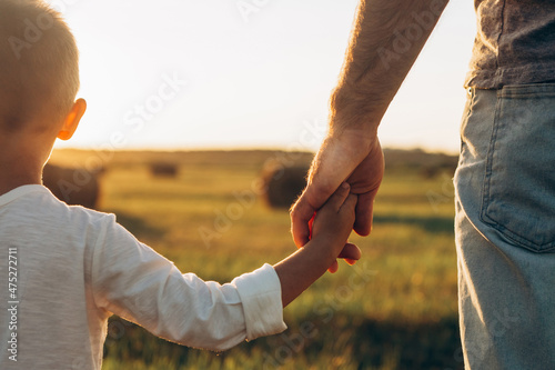 Father's and his son holding hands at sunset field. Dad leading son over summer nature outdoor. Family, trust, protecting, care, parenting concept photo