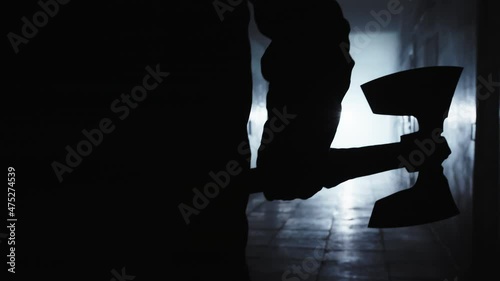 The gloomy figure of the executioner moves along the dark corridor towards the light. Only a figure is visible, he is holding a large double-sided ax, the man plunges into the light. photo