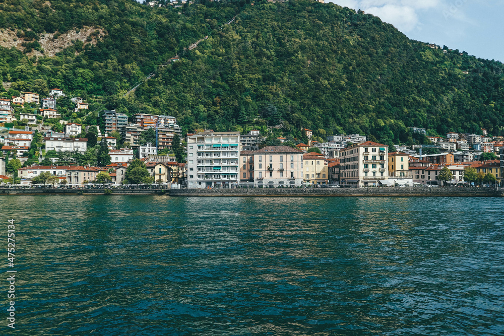 Panoramic view of big houses over hill town by the lake shore in northern Italy and boat passing 