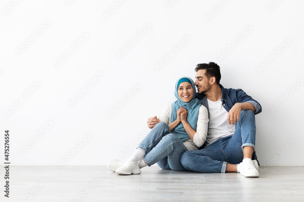 Joyful woman in hijab sitting on floor with her husband