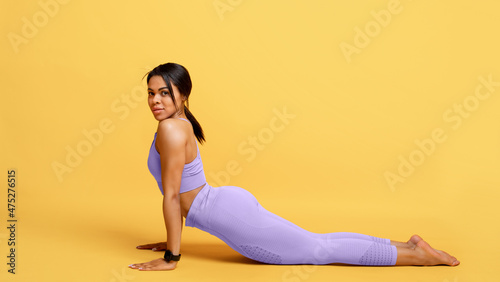 African american woman training, doing back stretching exercise at yellow studio background, panorama