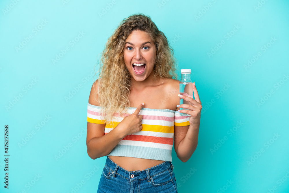 Young blonde woman with a bottle of water isolated on blue background with surprise facial expression Young blonde woman with a bottle of water isolated on blue background with surprise facial expression