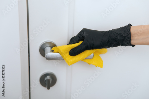 Cleaning door handle with yellow wipe in black gloves. Woman hand using towel for cleaning. Disinfection in hospital and public spaces against corona virus