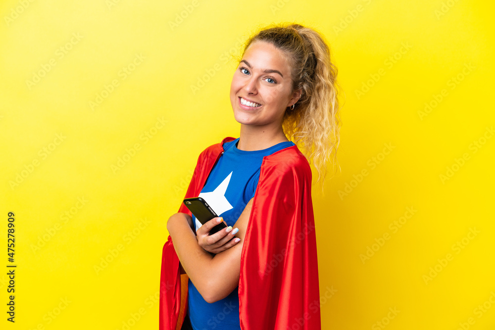 Super Hero woman isolated on yellow background holding a mobile phone and with arms crossed Super Hero woman isolated on yellow background holding a mobile phone and with arms crossed