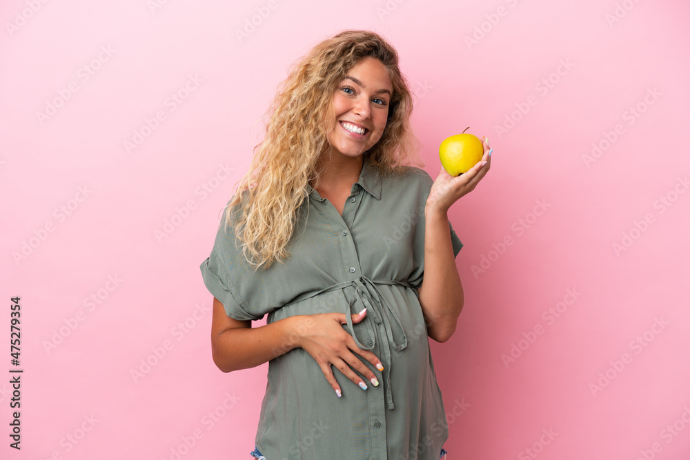 Girl with curly hair isolated on pink background pregnant and holding an apple Girl with curly hair isolated on pink background pregnant and holding an apple