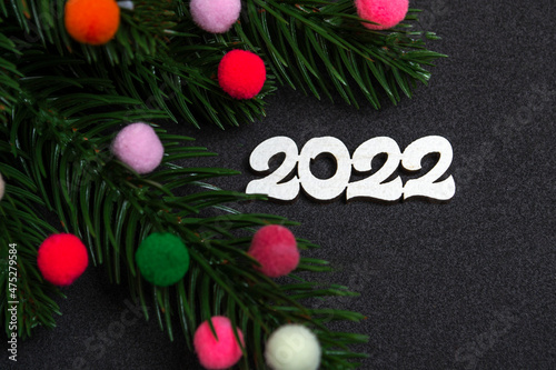 Christmas card. Flatley branches of a Christmas tree  colorful fur toys and the number 2022 on a black background.