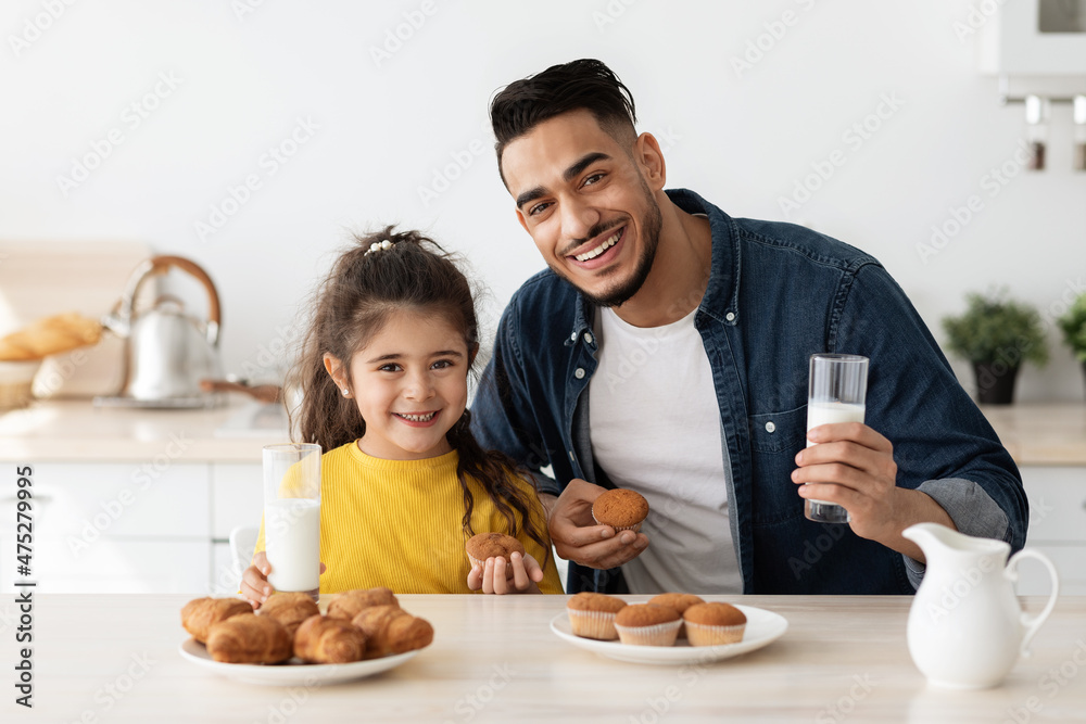Cheerful Arab Dad And His Little Daughter Having Snacks In Kitchen Cheerful Arab Dad And His Little Daughter Having Snacks In Kitchen