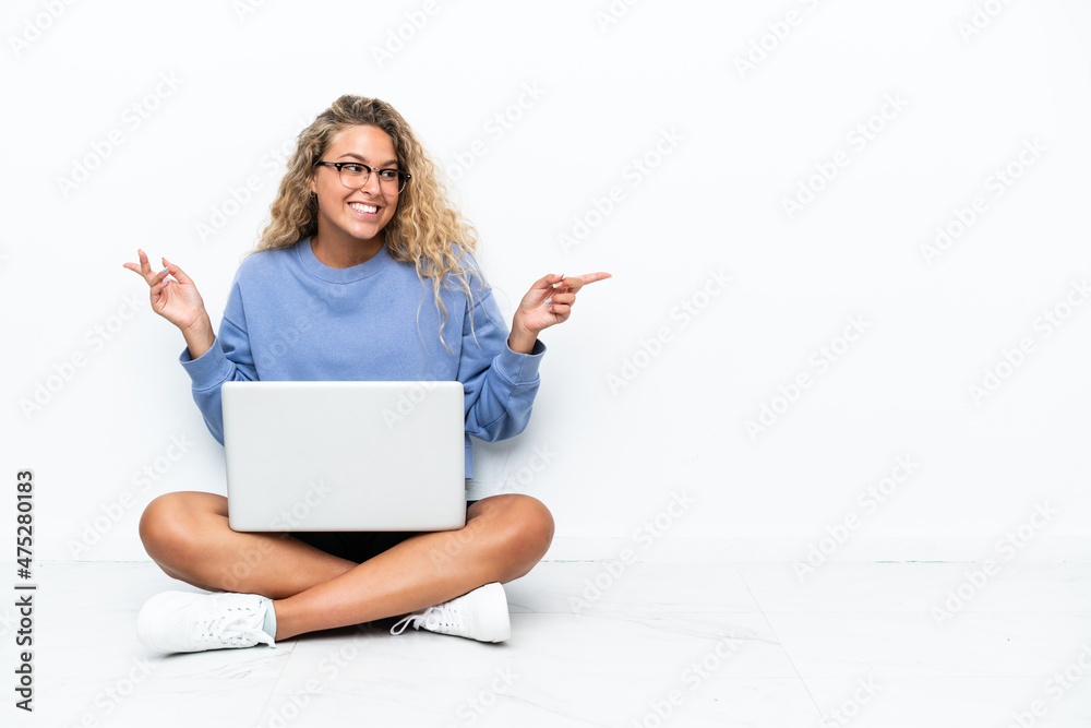 Naklejka premium Girl with curly hair with a laptop sitting on the floor pointing finger to the laterals and happy
