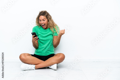 Girl with curly hair sitting on the floor surprised and sending a message