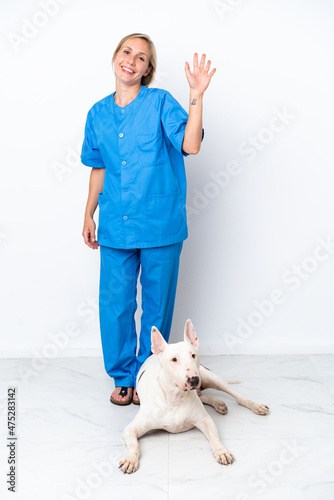 Young veterinarian English woman with dog isolated on white background saluting with hand with happy expression