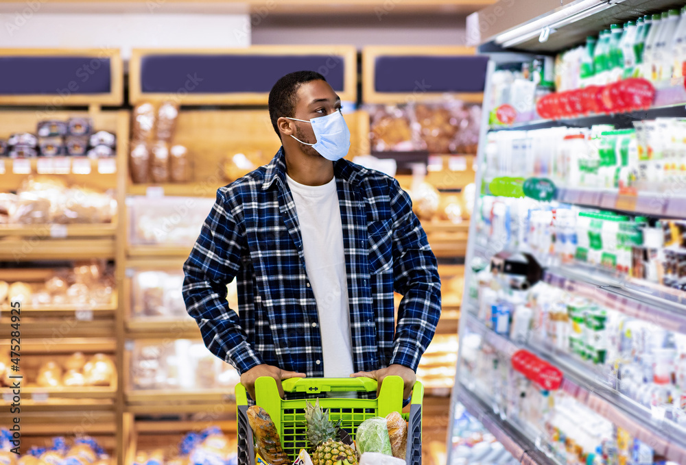 Young black guy in disposable face mask selecting dairy products at store during covid quarantine