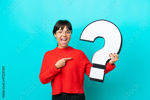 Young woman isolated on blue background holding a question mark icon with surprised expression