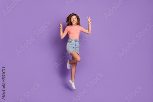 Full length body size view of attractive cheerful funky girl jumping showing v-sign isolated on vivid violet purple color background