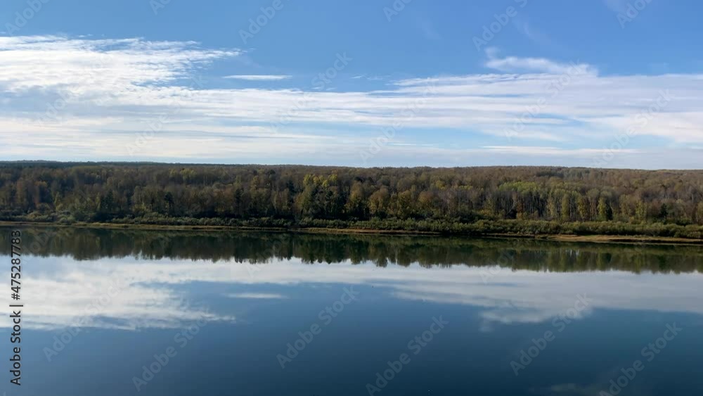Colorful foliage of trees and huge white clouds are reflected in the calm water of a pond or river on a beautiful autumn day. A quiet and beautiful place to relax. Colorful foliage of trees and huge white clouds are reflected in the calm water of a pond or river on a beautiful autumn day. A quiet and beautiful place to relax.