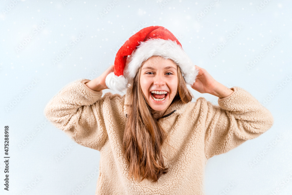 A beautiful little blonde girl in a red Christmas hat is smiling. Emotional child stands. Human emotions, facial expression A beautiful little blonde girl in a red Christmas hat is smiling. Emotional child stands. Human emotions, facial expression