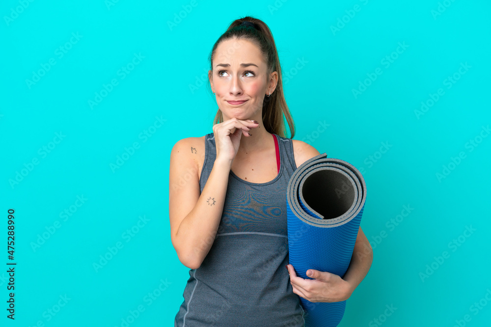 Young sport caucasian woman going to yoga classes while holding a mat isolated on blue background having doubts and thinking Young sport caucasian woman going to yoga classes while holding a mat isolated on blue background having doubts and thinking