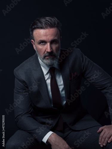 Portrait of adult businessman wearing trendy suit and sitting in modern studio on stylish chair against the black background © .shock