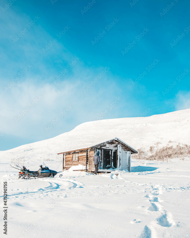 Tiny house in the mountains covered in snow with snowmobile in-front Tiny house in the mountains covered in snow with snowmobile in-front