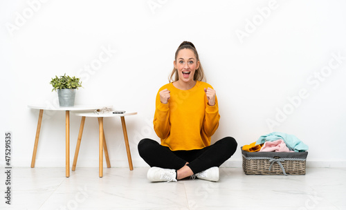 Young caucasian woman folding clothes sitting on the floor isolated on white background celebrating a victory in winner position