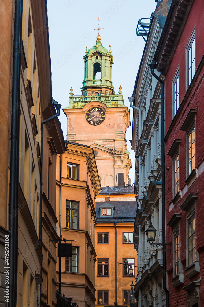 Fototapeta premium Low-angle view of historical buildings on the Stora Gramunkegrand Alley and the tower of the Saint Nicholas Church in winter day at sunset, Stockholm, Sweden 