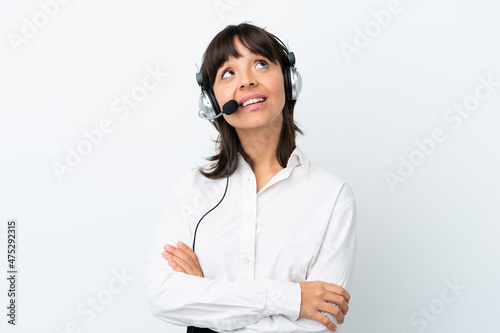 Telemarketer mixed race woman working with a headset isolated on white background looking up while smiling