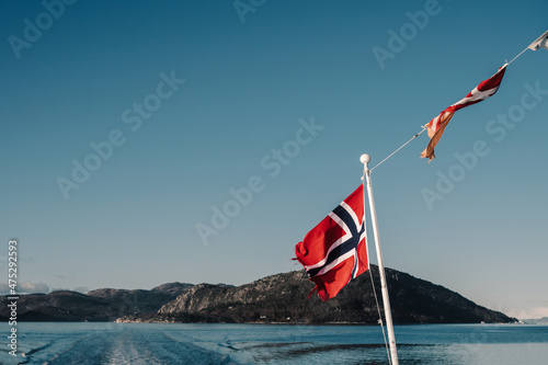 Waving flag of Norway on background of fjord and rocks. Cruise along Lusefjord on a sunny day. Luxury tourism.