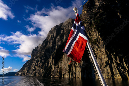 Waving flag of Norway on background of fjord and rocks. Cruise along Lusefjord on a sunny day. Luxury tourism.