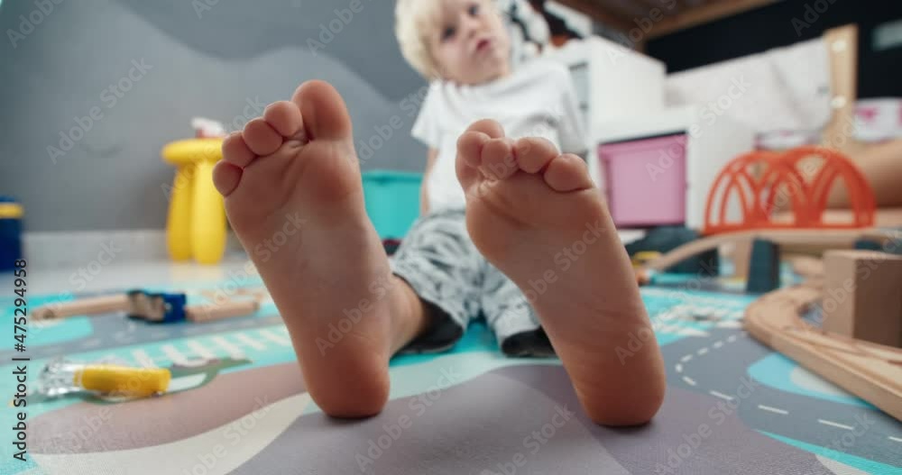 Closeup of cute child foot moving fingers laying on the floor in home barefoot. Carefree childhood enjoying in kid room after playing with toys