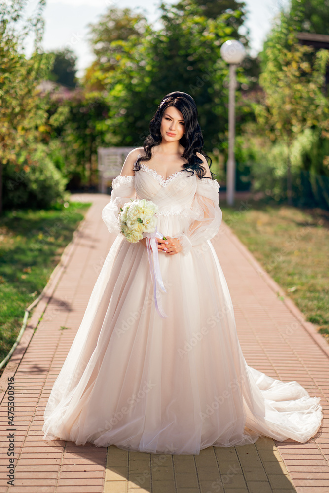 brunette bride in a dress with a bouquet of flowers on the path in the park.