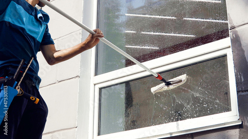 Male professional cleaning service worker in overalls cleans the windows and shop windows of a store with special equipment