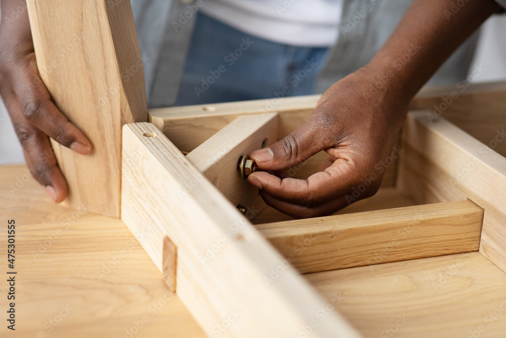 Self-assembly furniture concept. Black man screwing bolt to wooden table, installing desk by yourself at home, closeup Self-assembly furniture concept. Black man screwing bolt to wooden table, installing desk by yourself at home, closeup