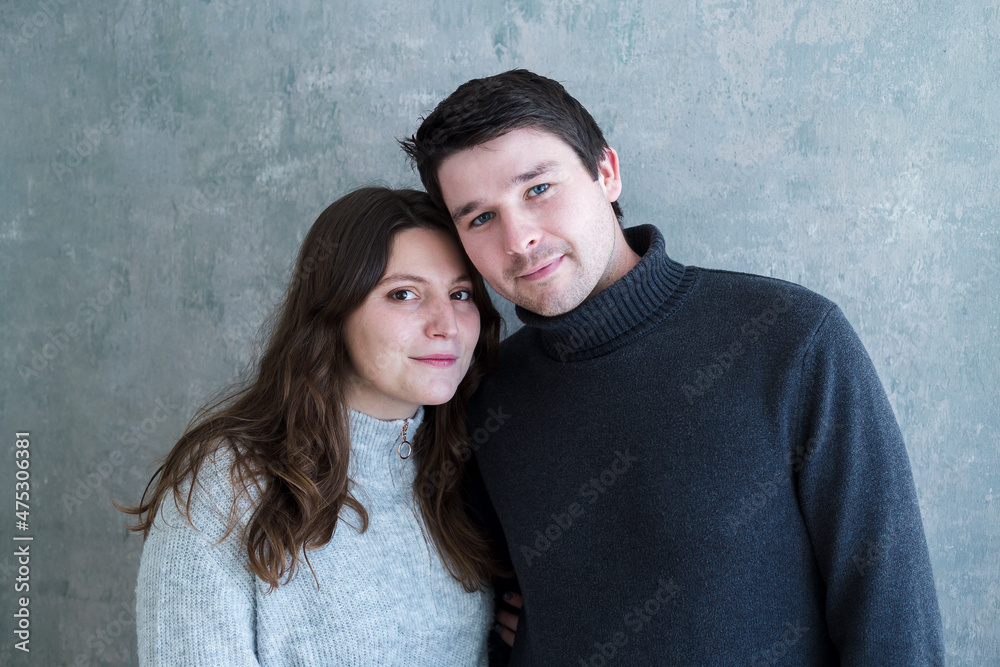 Medium horizontal portrait of cute young couple in casual sweaters standing together against plain background