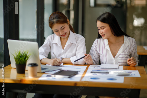 Two female colleagues working together on the project with a laptop in the modern office. doing finances, accounting analysis, report data pointing graph Freelance education and technology concept.