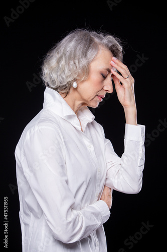 Side view portrait of an old but modern trendy woman suffering from a headache or migraine holding her head in her hands with a desperate expression isolated on black background
