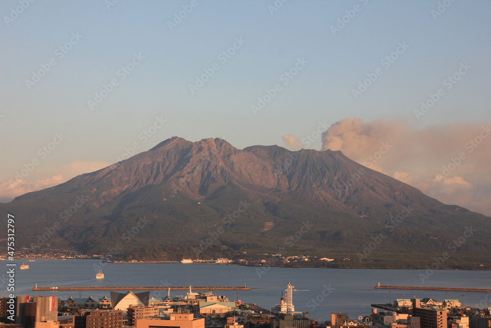 鹿児島市内の城山か錦江湾と桜島を望む。夕焼けに赤く染まながら噴煙を上げる桜島。