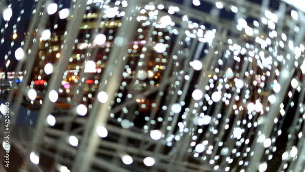 Bright white lights out of focus flashing against a winter festively decorated street. Christmas light decorations of a city street. Bright white lights out of focus flashing against a winter festively decorated street. Christmas light decorations of a city street.