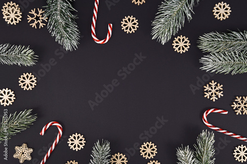 Winter fir branches, candy canes and snowflakes forming border around black background with copy space