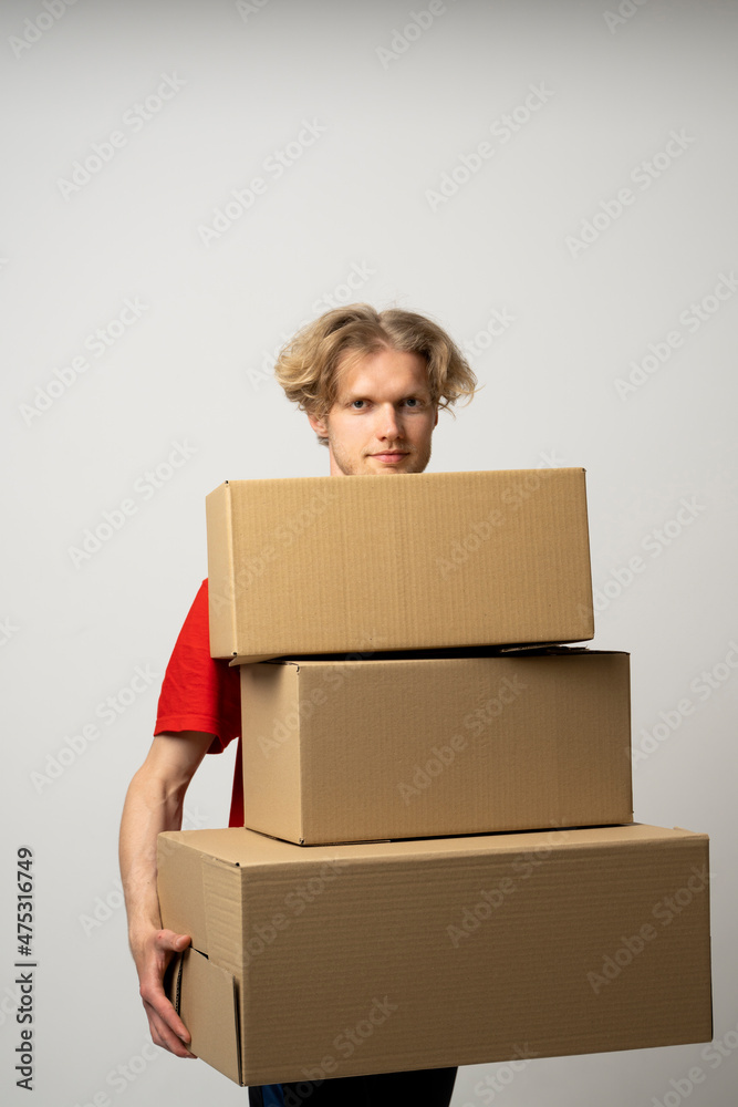 Delivery man in a red uniform holding a stack of cardboard boxes. Courier delivering postal packages over white studio background. Delivery man in a red uniform holding a stack of cardboard boxes. Courier delivering postal packages over white studio background.